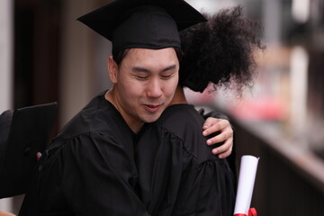 Two graduates in caps and gowns beam with joy, embracing and cheering in celebration. Their wide...