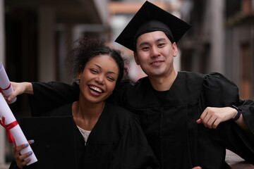 Two graduates in caps and gowns beam with joy, embracing and cheering in celebration. Their wide...
