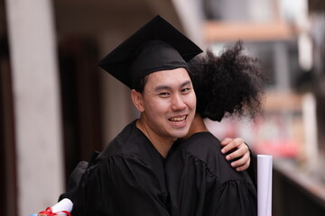Two graduates in caps and gowns beam with joy, embracing and cheering in celebration. Their wide...