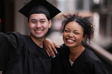Two graduates in caps and gowns beam with joy, embracing and cheering in celebration. Their wide...