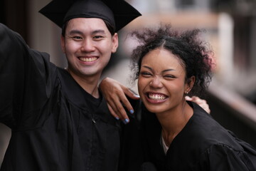 Two graduates in caps and gowns beam with joy, embracing and cheering in celebration. Their wide...