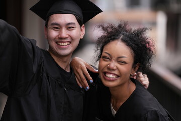 Two graduates in caps and gowns beam with joy, embracing and cheering in celebration. Their wide...