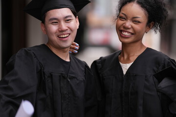 Two graduates in caps and gowns beam with joy, embracing and cheering in celebration. Their wide...