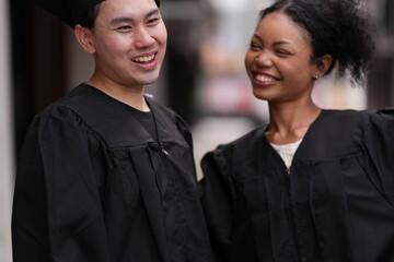 Two graduates in caps and gowns beam with joy, embracing and cheering in celebration. Their wide...