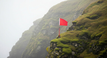 Naklejka premium Red flag stands on mossy cliff with foggy mountain backdrop