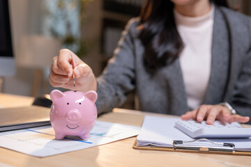 A woman is putting coins into a pink piggy bank