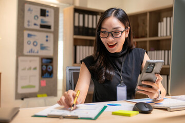 A woman is sitting at a desk with a cell phone in her hand