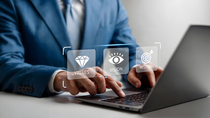 Focused entrepreneur in suit utilizing laptop highlighting core values, vision, and mission for strategic business planning and goal setting in modern corporate setting.