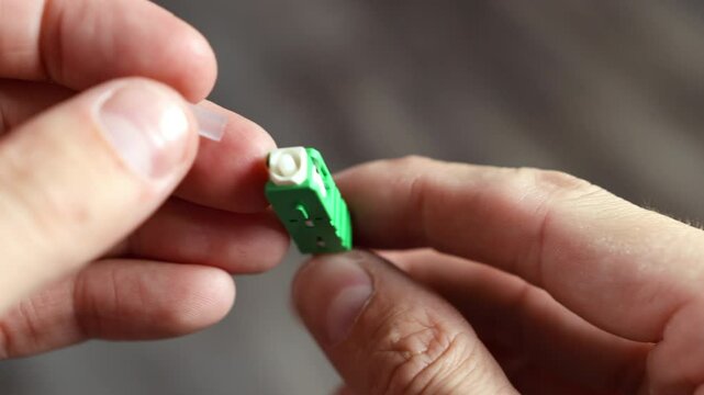 Demonstration of an APC fiber optic connector connected to a cable, showing rotation and opening of the protective cap where light passes through 