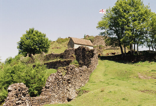 Historic stone ruins with a house and Georgian flag on a sunny day 