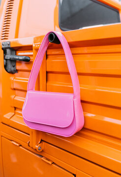 Stylish pink handbag hanging on orange truck surface