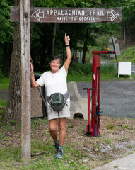 Middle aged female hiker poses next to a sign marking the Appalachian Trail in Delaware Water Gap, Pennsylvania