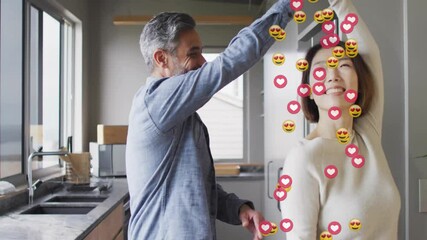 Lifestyle couple with man lifting partner hand causing twirl in kitchen with floating heart emojis