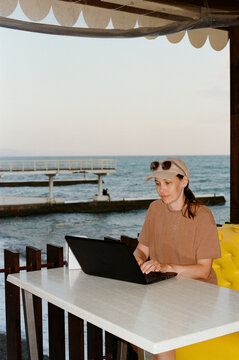 MIddle aged woman using laptop at street cafe by seaside.