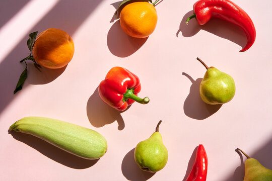 Bell pepper, pear, squash and oranges making pattern on pink backdrop.