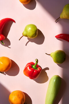 Bell pepper, pear, squash and oranges making pattern on pink backdrop.