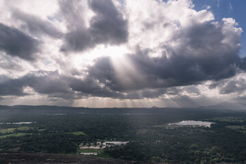 Sunbeams filtering through dark clouds, illuminating a lush green landscape in Sri Lanka, create a...