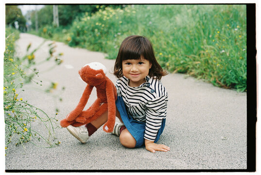 Smiling Child Sitting on Path with Plush Toy