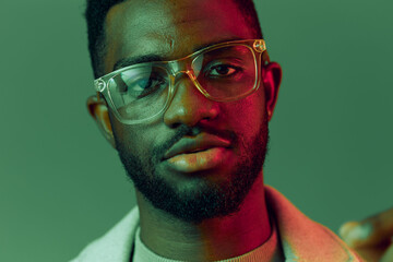 Portrait of a young Black man with glasses, expressing confidence against a vibrant green and pink...