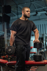 male athlete stands confidently holding dumbbell while preparing for a strength training session in...