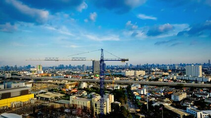 A construction crane stands tall amidst the bangkok cityscape under blue skies