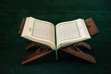 Open Quran on a wooden stand, placed on a dark green prayer rug
