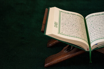 Open Quran on a wooden stand, placed on a dark green prayer rug