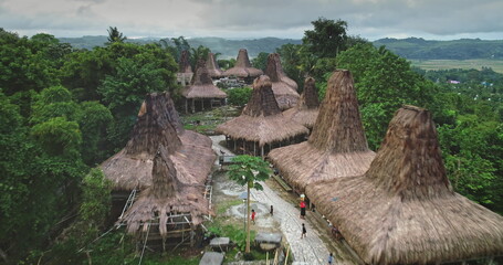 Aerial view of unique custom houses with high, thatched roofs forming a captivating ancient village in a remote area of Sumba island, Indonesia, with local people walking on a path