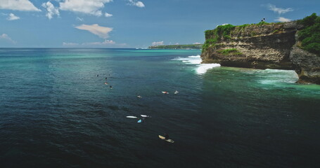 Group of surfers waiting for waves near a cliff at Dreamland Beach, Bali, Indonesia, aerial drone view of a beautiful sunny day with blue sky and clouds