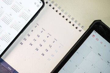 Flatlay of smartphone and tablet displaying digital calendars beside a paper calendar