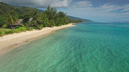 Stunning aerial view of a tropical beach with crystal-clear turquoise water gently lapping against the shore, inviting tourists to swim and relax amidst lush green vegetation and palm trees