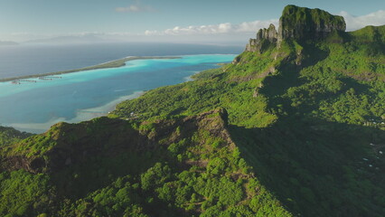 Aerial drone of stunning beauty Bora Bora tropical island, green forest vegetation, turquoise lagoon, and majestic mount Otemanu under a clear blue sky. Wild travel destination, remote nature