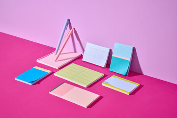 Artistic arrangement featuring vibrant notepads and pens on pink table