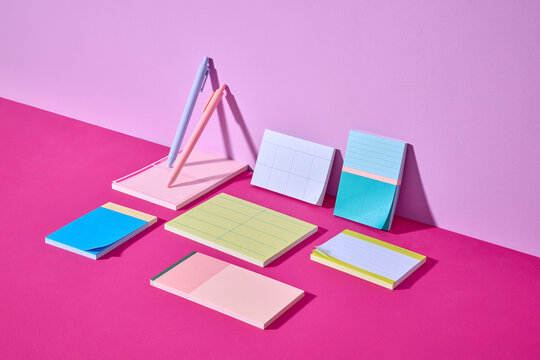 Artistic arrangement featuring vibrant notepads and pens on pink table