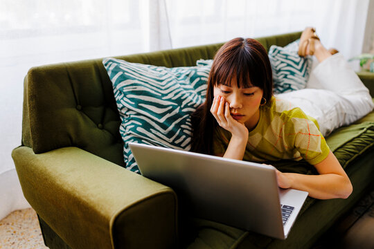 Woman using laptop while lying on sofa 