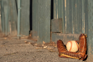 Baseball and mitt leaning against the worn green fence of a vintage ball park.