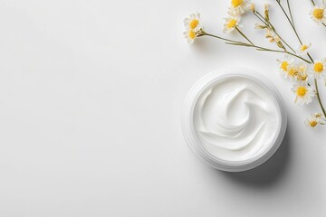 Cream jar, chamomile flowers, white background.  Atop a pristine white surface, a white jar of creamy lotion is gently swirled.  Delicate chamomile blossoms surround the jar