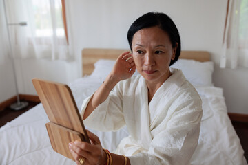 Woman in robe looks in mirror at her bedroom.