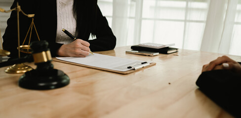 Two professionals are signing a legal agreement at a desk, with a judge’s gavel nearby. The scene...