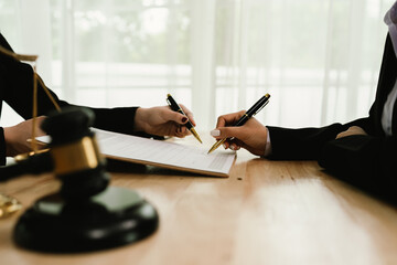 Two professionals are signing a legal agreement at a desk, with a judge’s gavel nearby. The scene reflects law, business contracts, and formal documentation.x