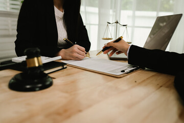 Two professionals are signing a legal agreement at a desk, with a judge’s gavel nearby. The scene reflects law, business contracts, and formal documentation.x