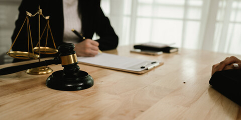 Two professionals are signing a legal agreement at a desk, with a judge’s gavel nearby. The scene...