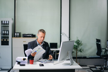 Confident businessman working on finance analysis with a tablet and laptop at office desk. Perfect for business