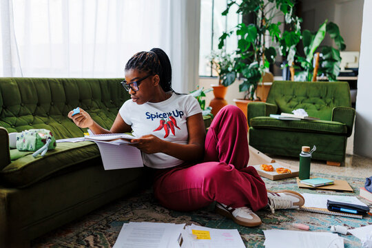 Female student reviewing notes and highlighting key points at home