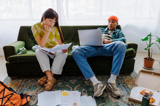 Students using laptop and reading documents in messy living room
