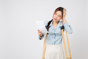 Crutches support sad Asian woman leg or foot broken holding bill paper, confused and counting payment, leaning on crutches after injury and worried about over money. isolated studio white background