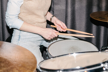 A young woman in blue jeans plays the drums.