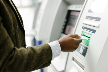 Anonymous black man using ATM, close up image on hand with a bank card
