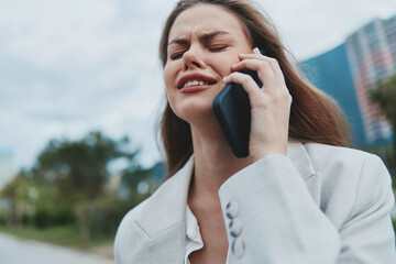 upset woman talking on phone outdoors expressing stress and frustration in casual white blazer...