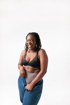 Laughing woman struggles with jeans, bra, and shapewear.
